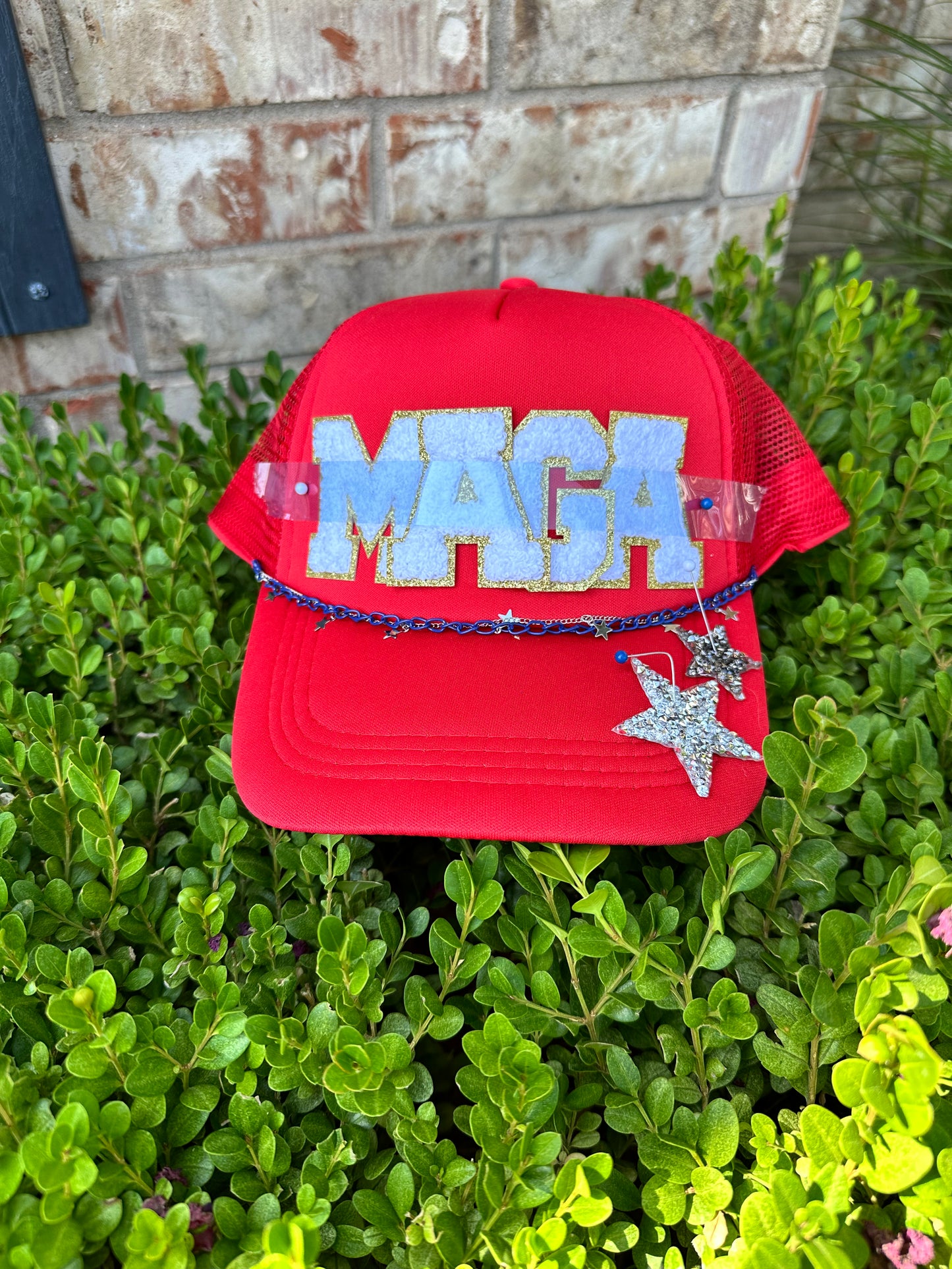 Red trucker hat with the letters MAGA, 2 star patches, blue chain, and sliver star chain