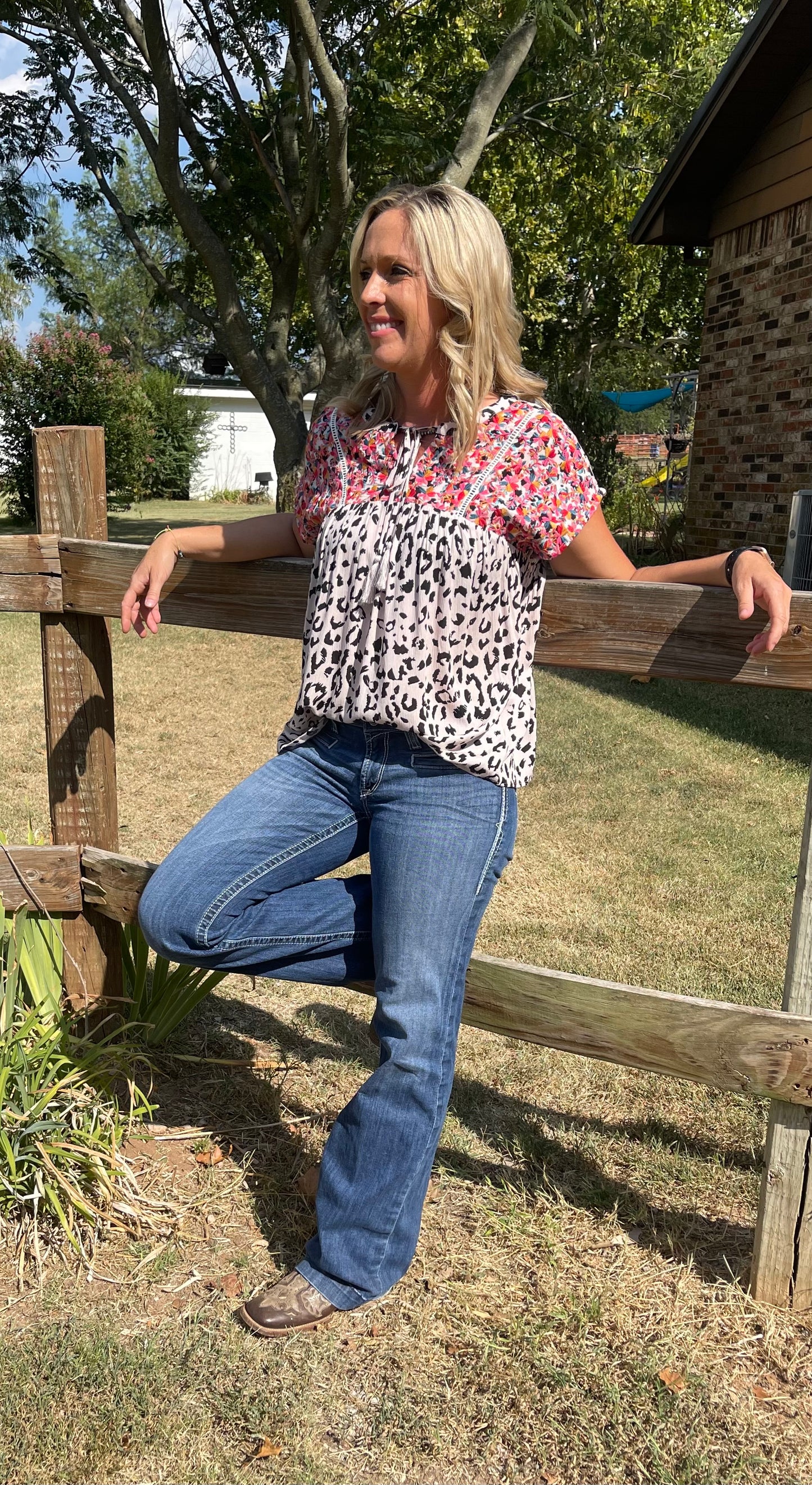Woman wearing a black and white cheetah blouse with colorful embroidery and tassel tie in size small
