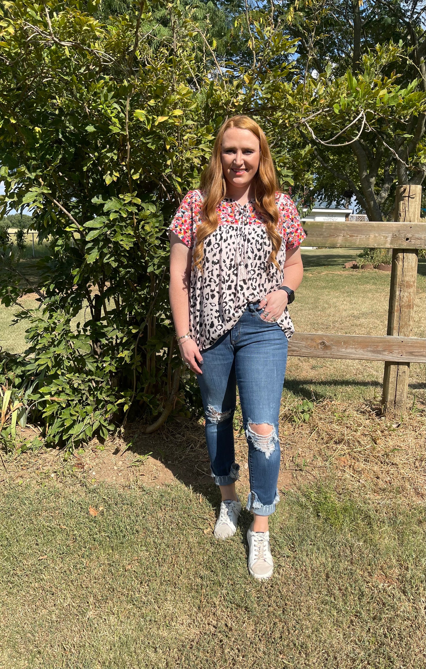 Woman wearing a black and white cheetah blouse with colorful embroidery and tassel tie in size Large