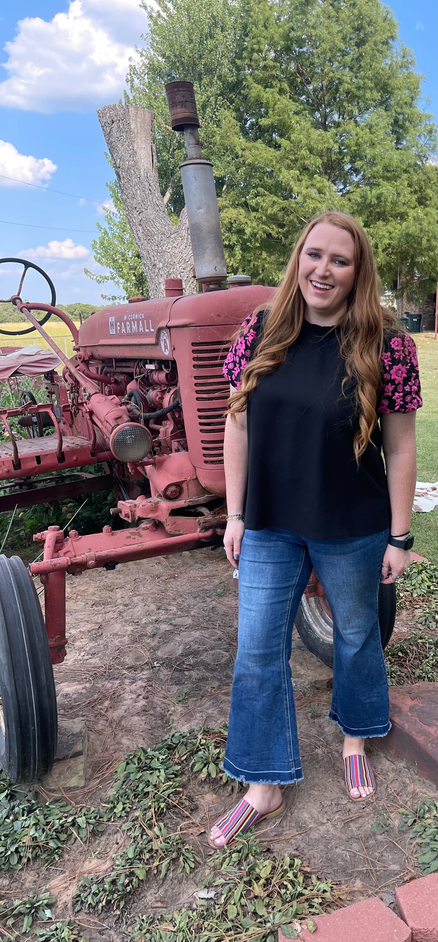 Woman wearing a black short puff sleeve shirt with pink embroidered flowers on the sleeves in a size Large, and flare legged denim capri pants