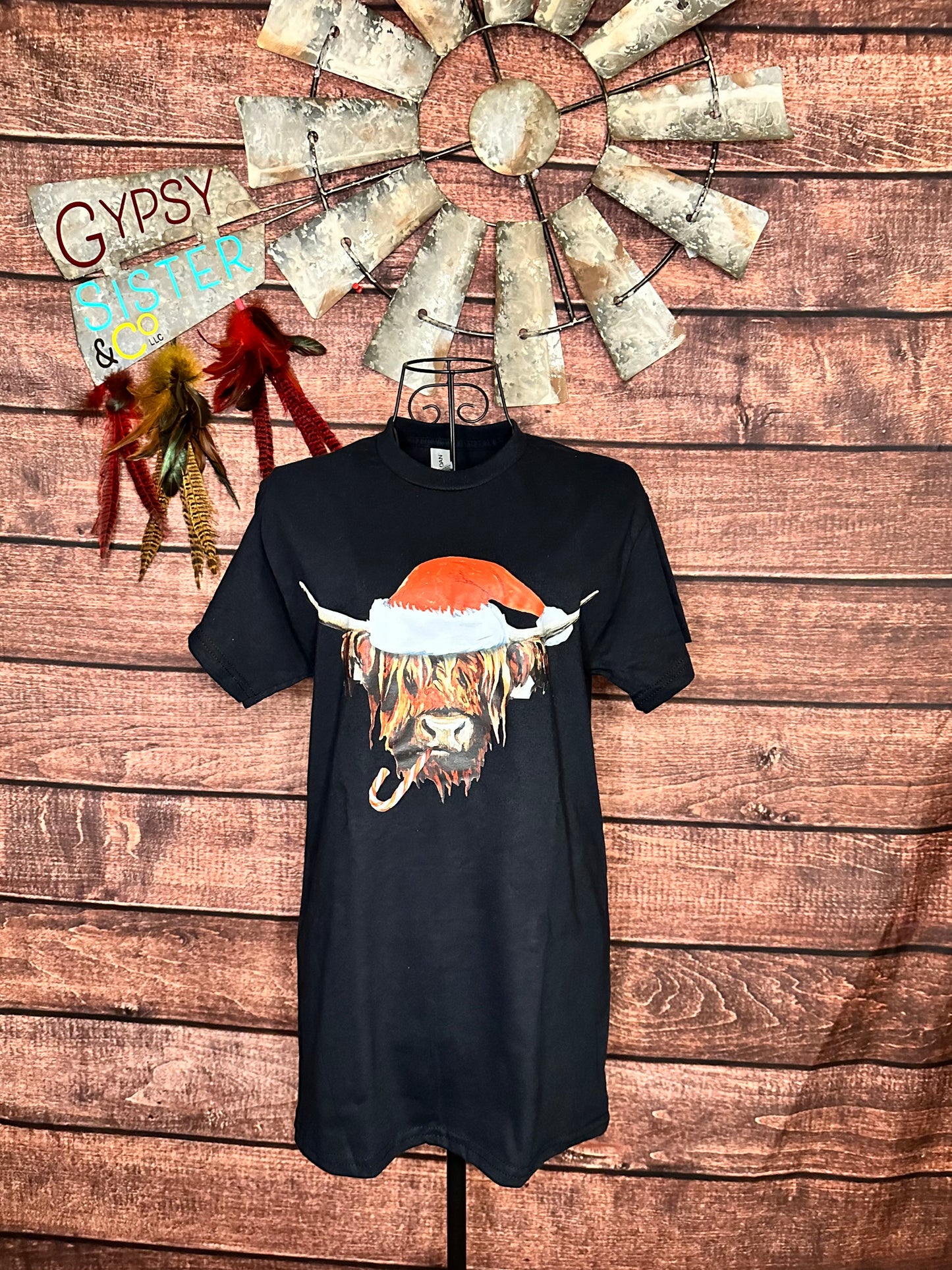 Black short sleeve t-shirt with brown Highland cow wearing a Santa hat and chewing on a candy cane