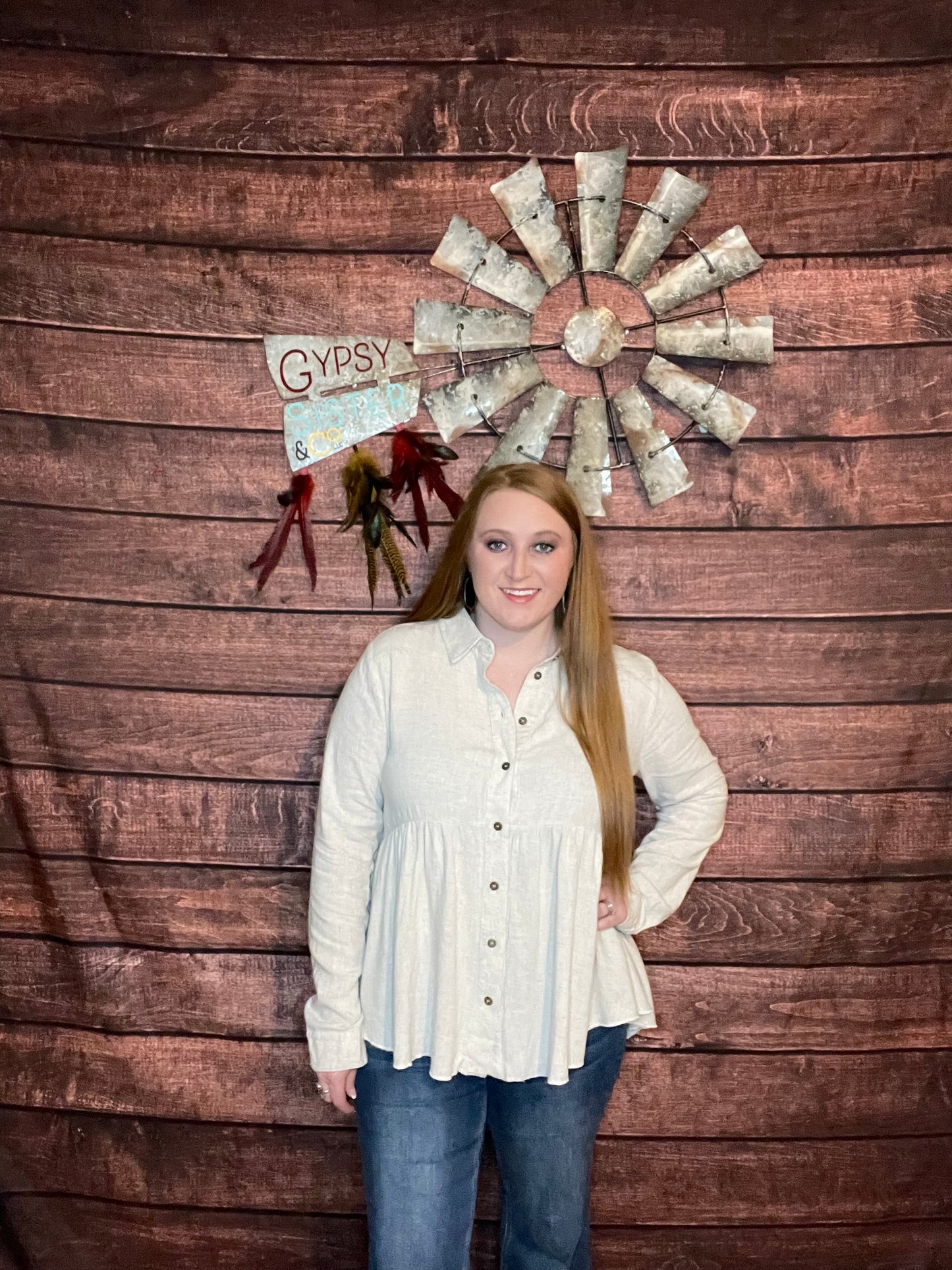 Model wearing oatmeal colored babydoll button down top with ruffled high low hem