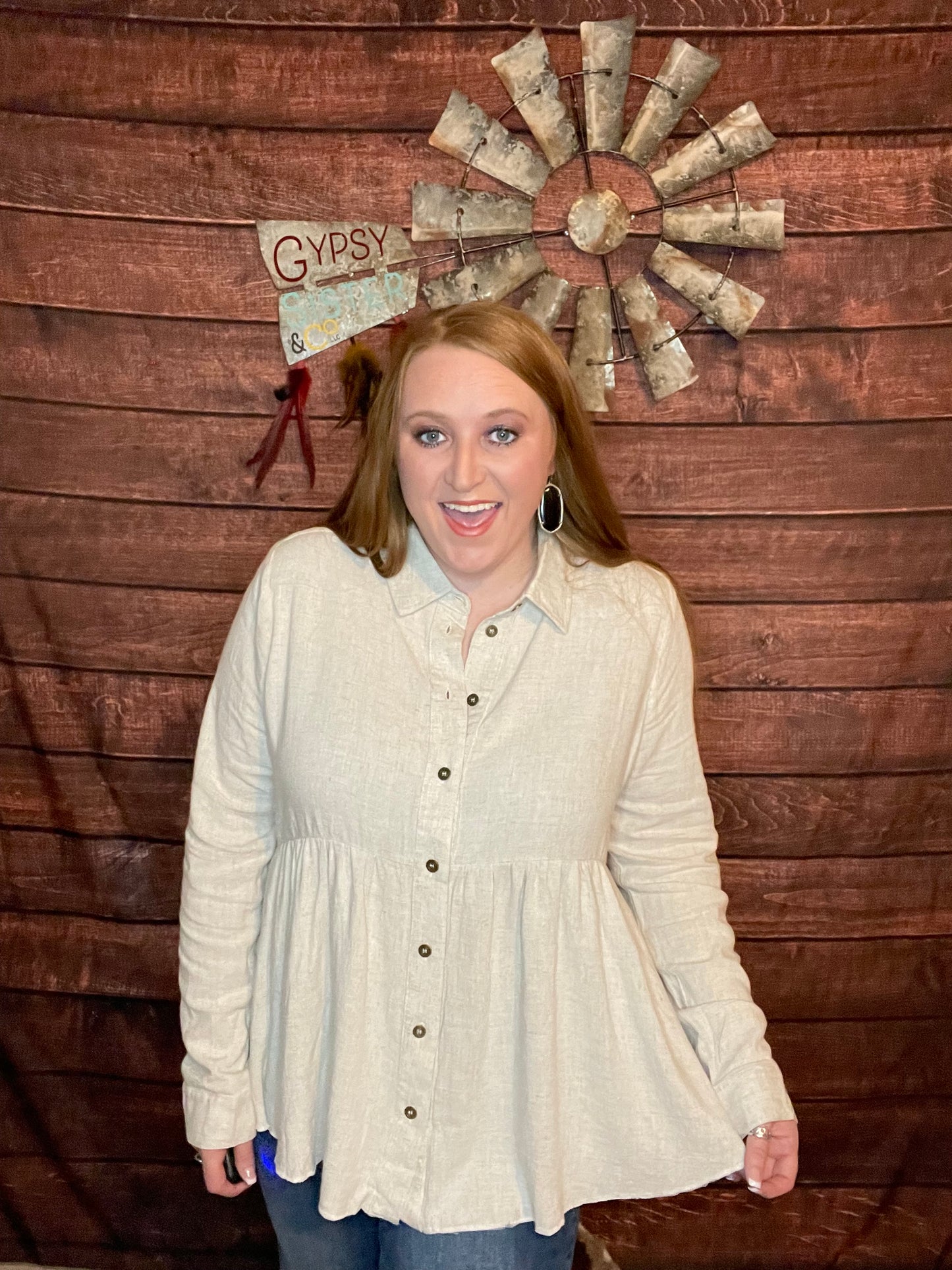 Model wearing oatmeal colored babydoll button down top with ruffled high low hem