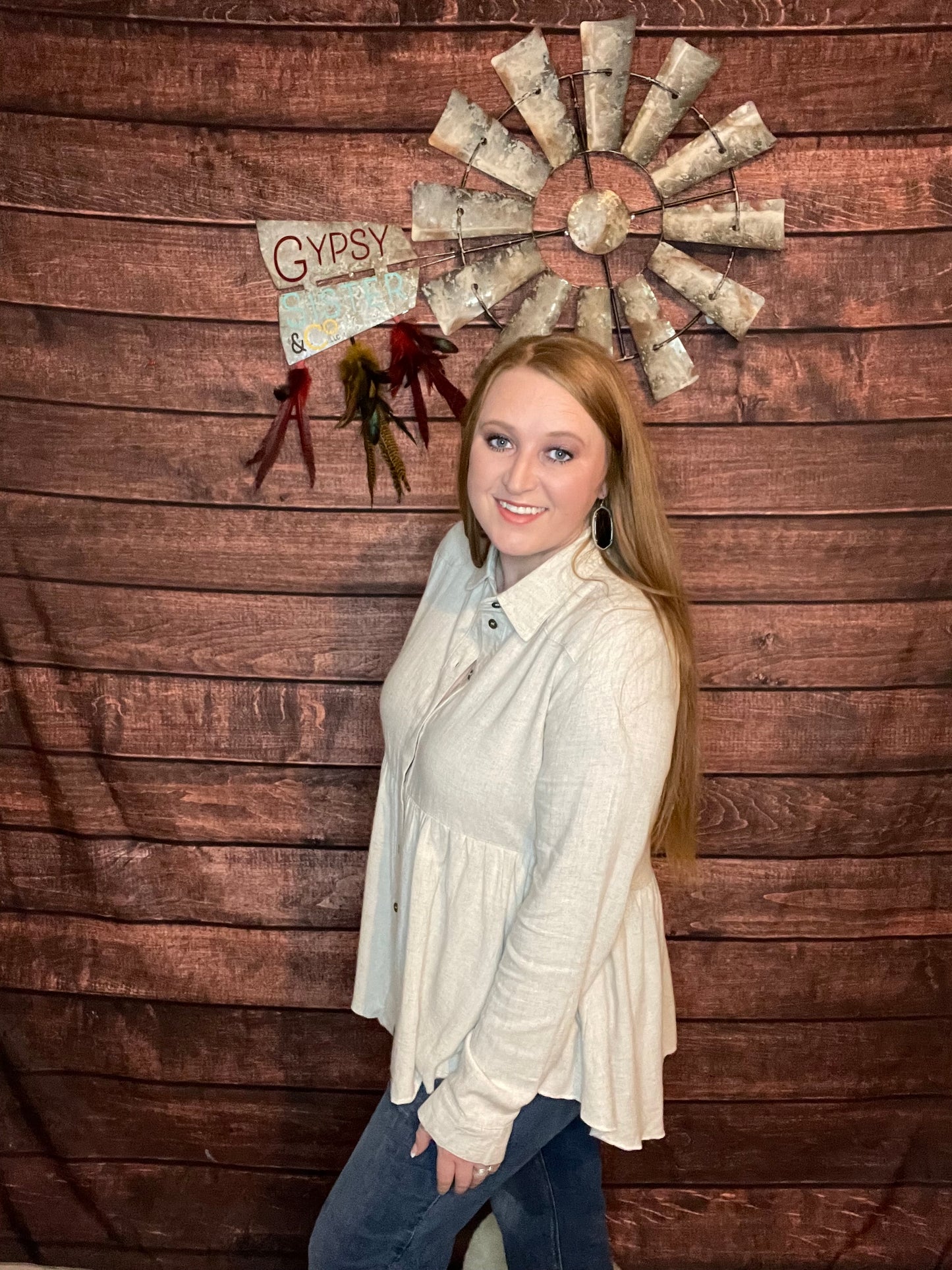 Side view of Model wearing oatmeal colored babydoll button down top with ruffled high low hem