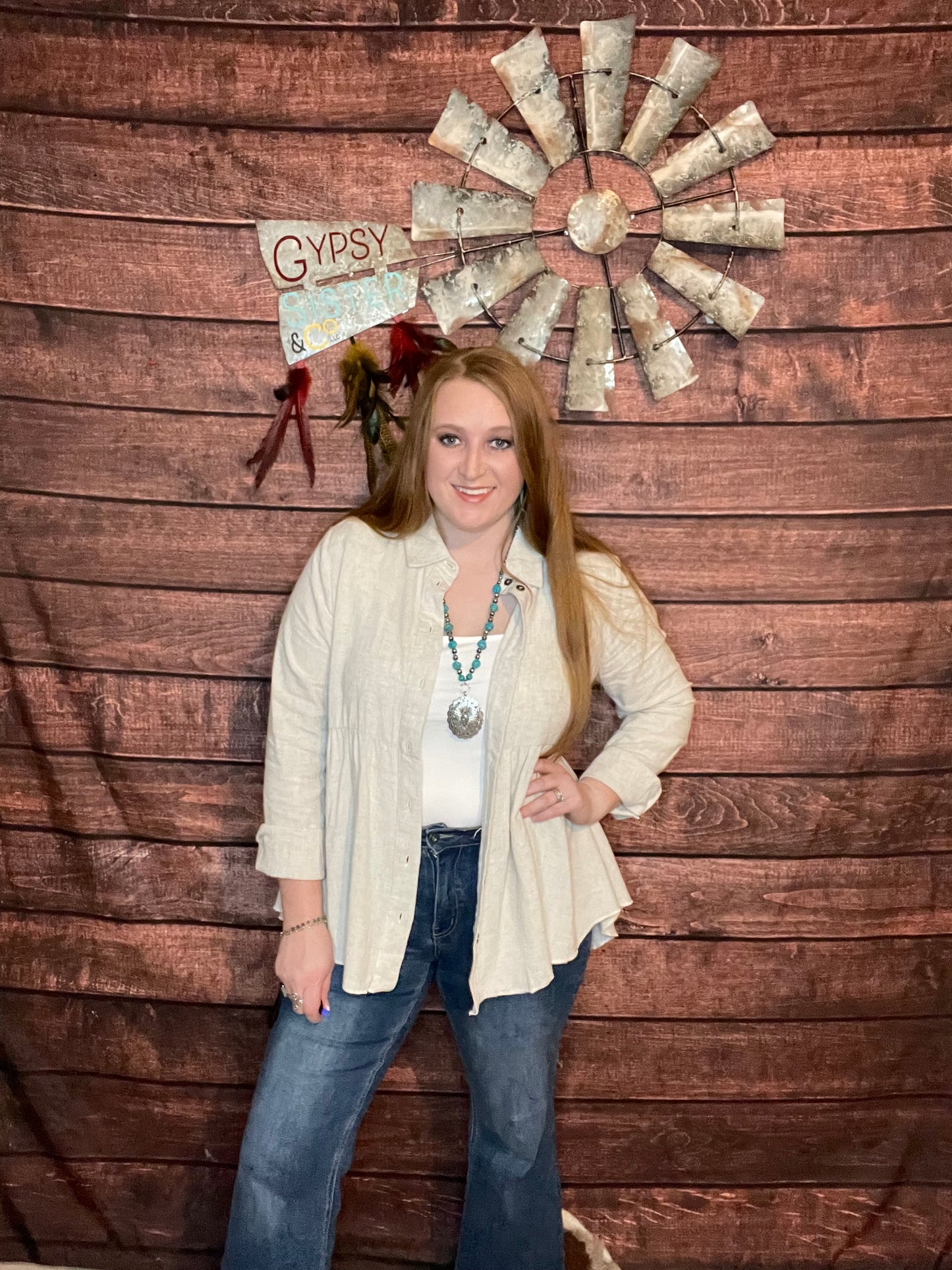 Model wearing oatmeal colored babydoll button down top with ruffled high low hem with as a "shacket" with jeans