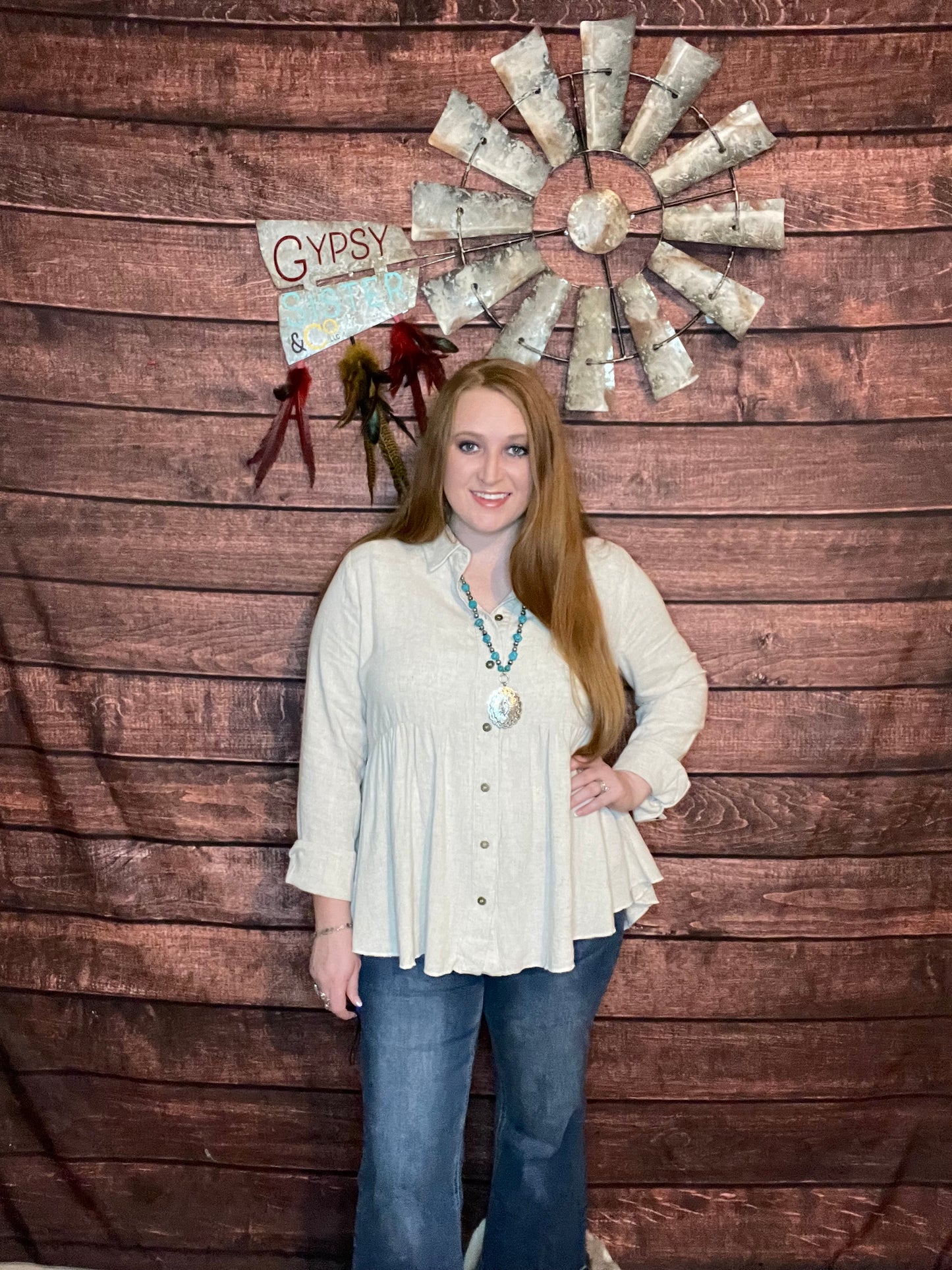Model wearing oatmeal colored babydoll button down top with ruffled high low hem with jeans and turquoise jewelry