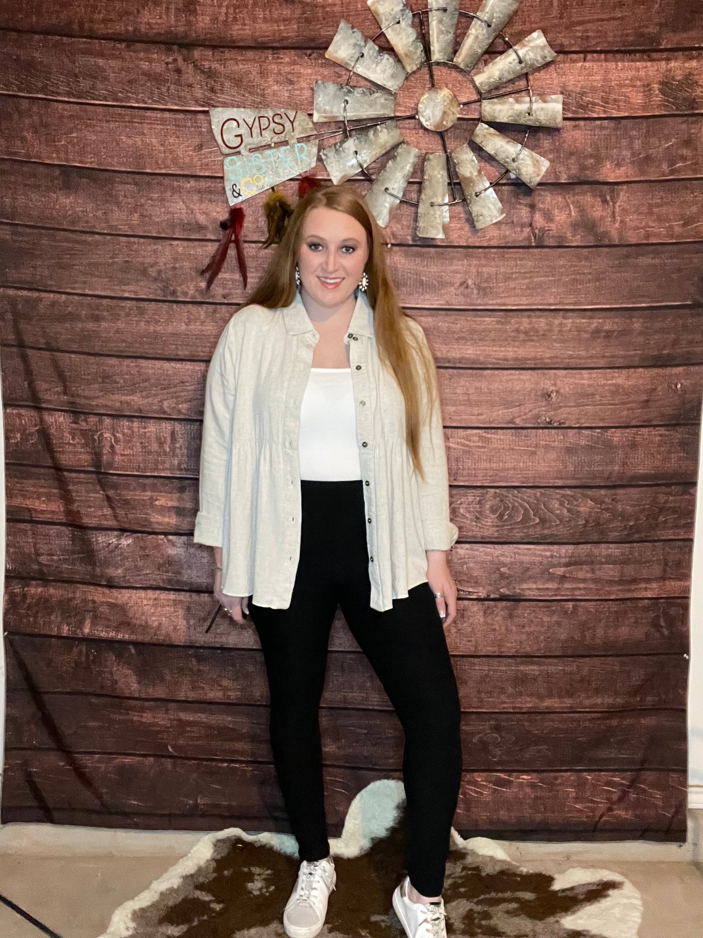 Model wearing oatmeal colored babydoll button down top with ruffled high low hem with leggings