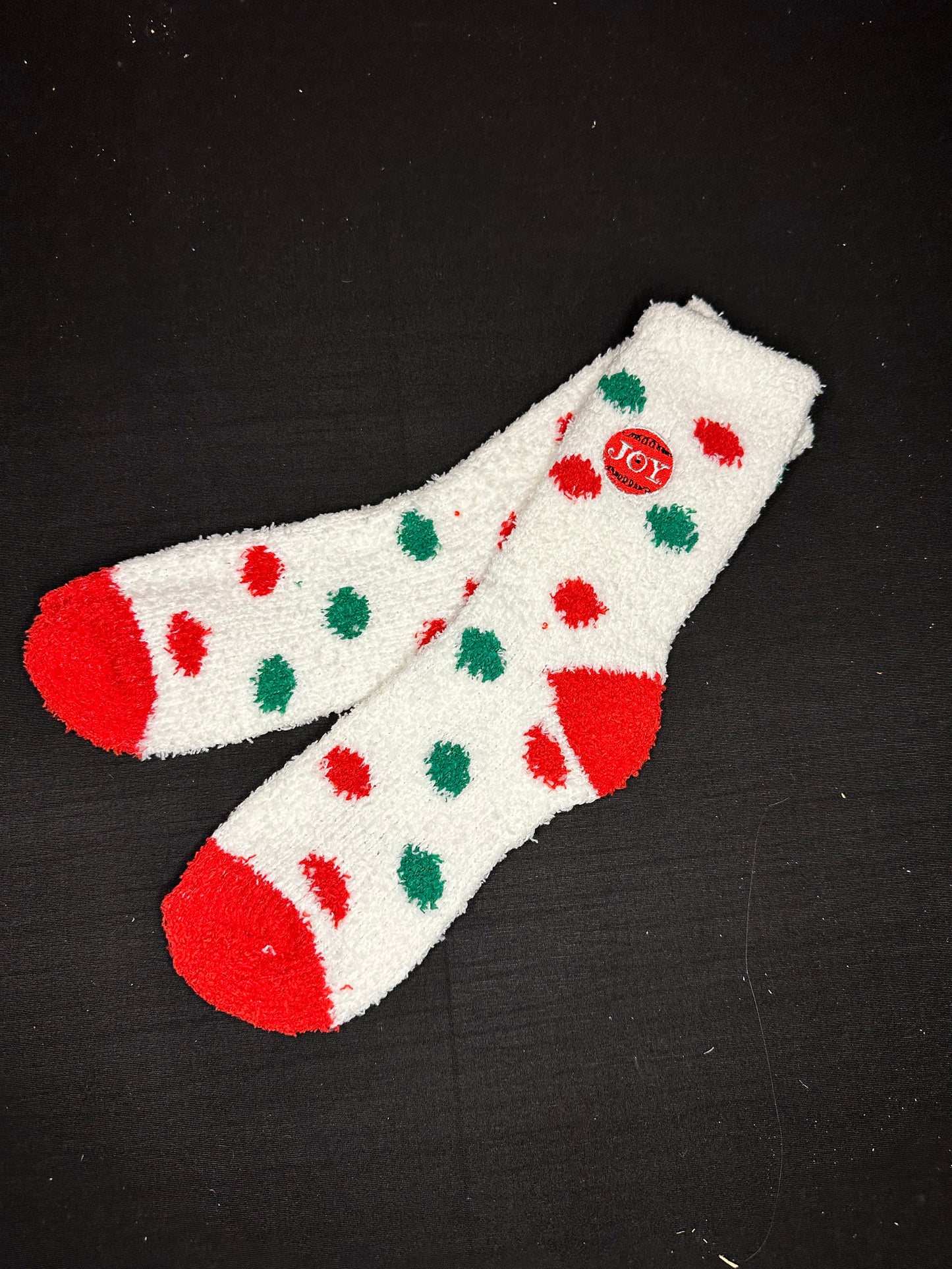 White fuzzy socks with green and red polka dots and an embroidered ornament that says "JOY"