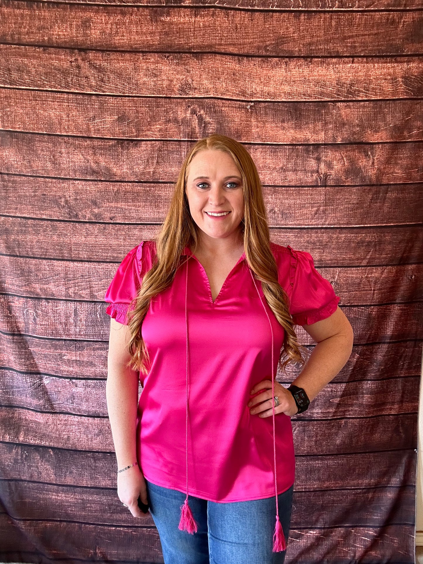 Model wearing bright pink short sleeve blouse with a shiny satin like finish with jeans