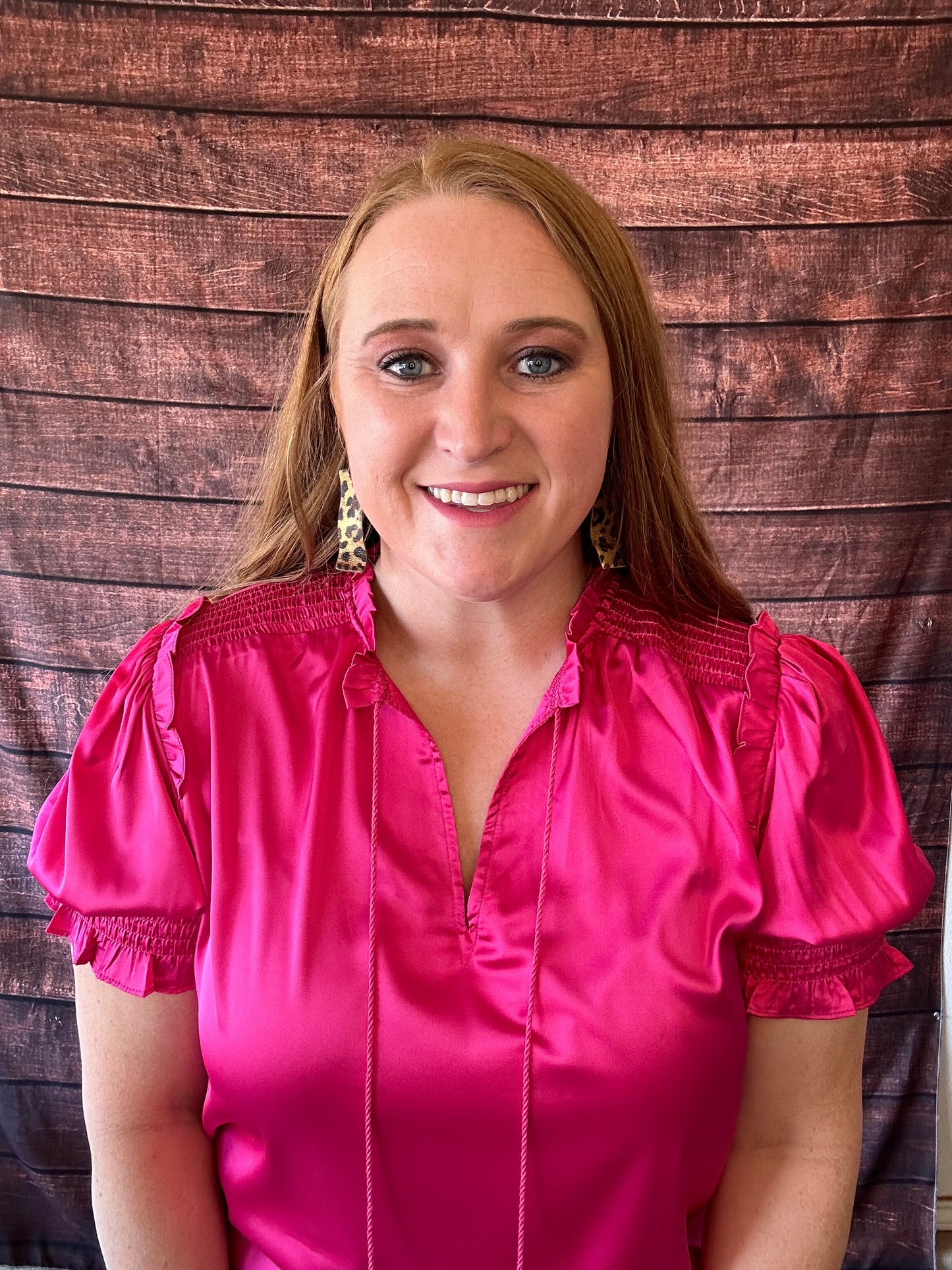 Model wearing bright pink short sleeve blouse with a shiny satin like finish showing detailing on the sleeves and shoulders