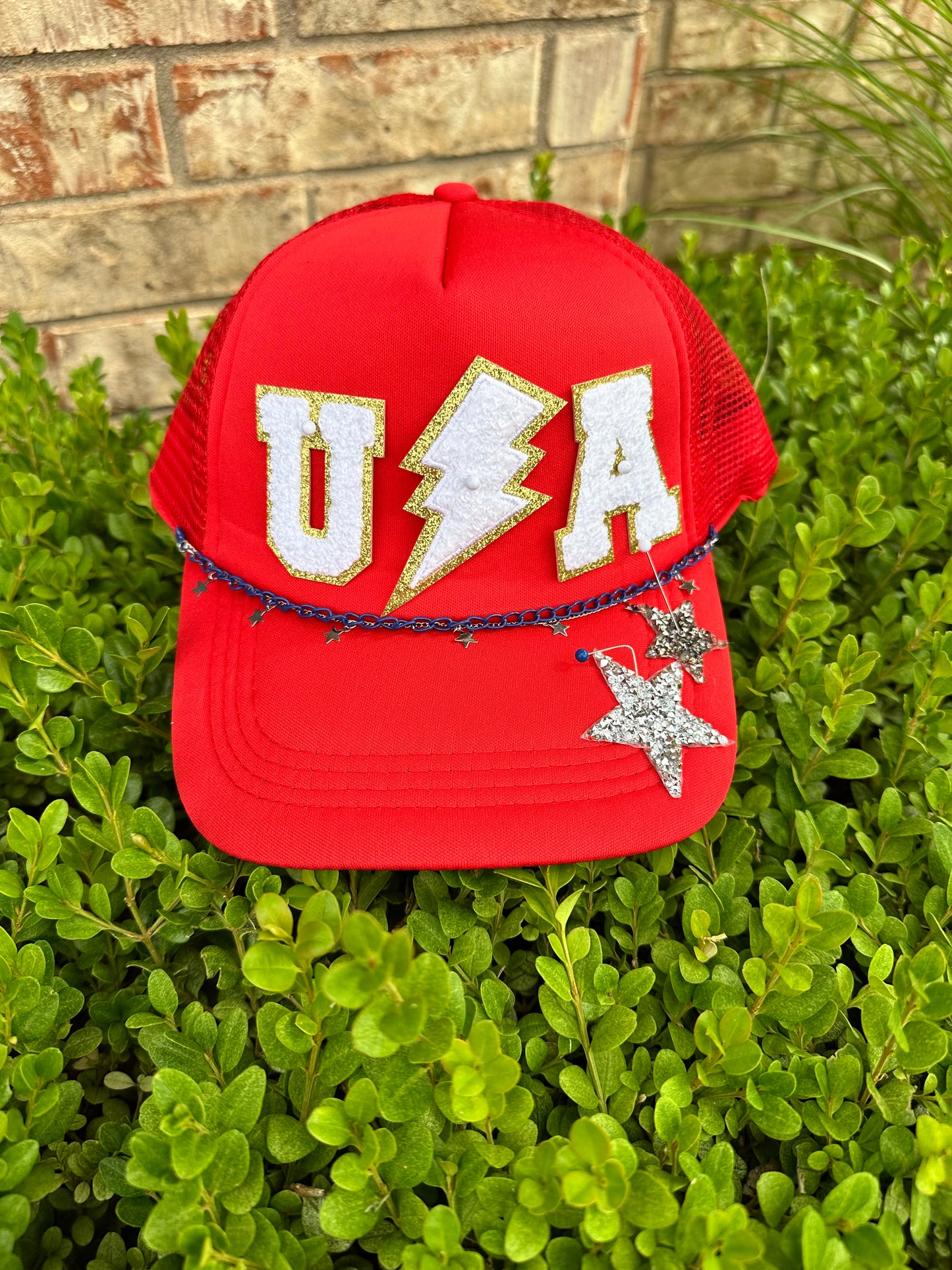 Red Trucker hat that has U, lightning bolt, A, 2 star patches and 2 chains