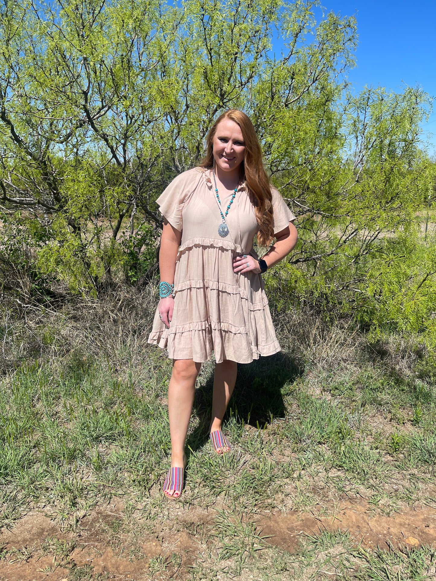 Model wearing ruffle tiered khaki dress with serape print sandals