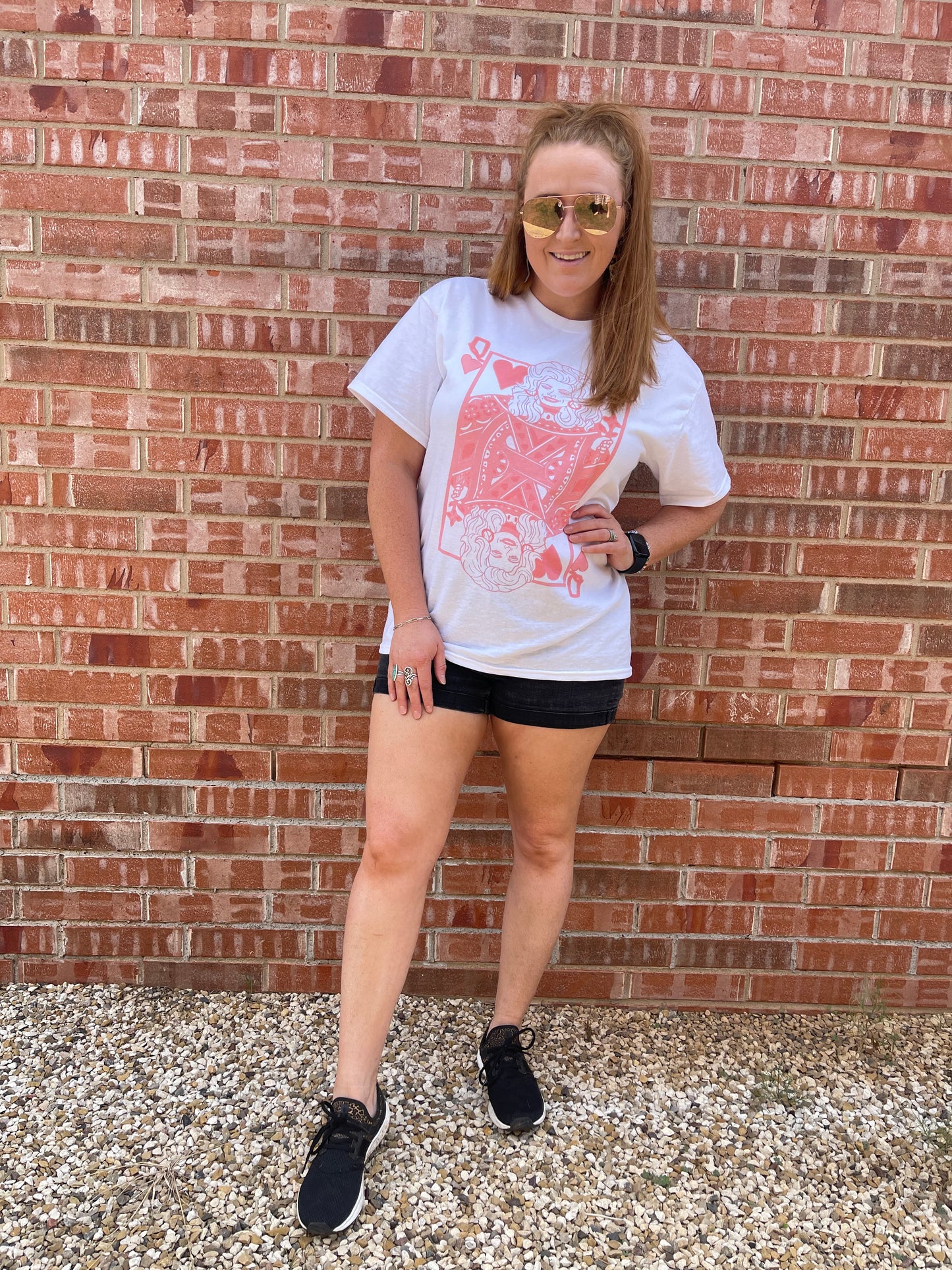 Model wearing Queen of Hearts shirt with black shorts, black tennis shoes, and pink sunglasses