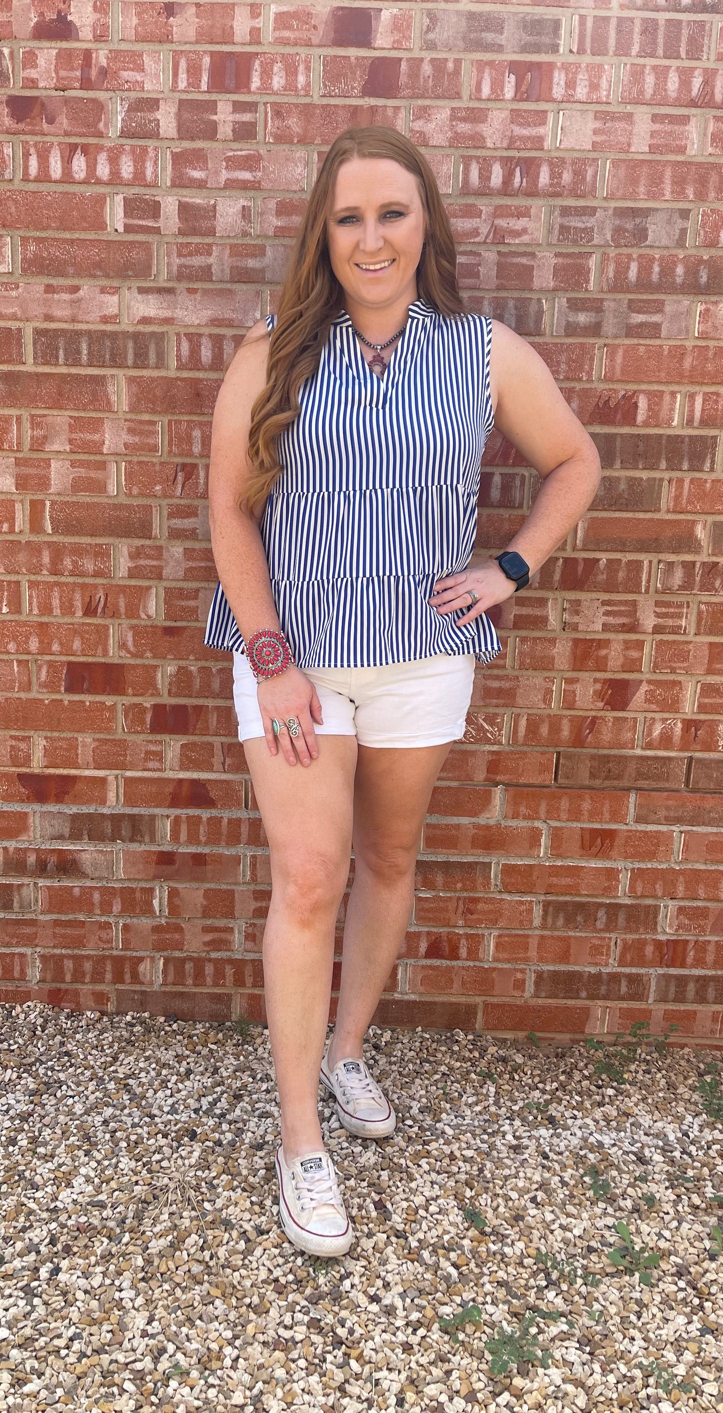 Model wearing blue and white striped sleeveless blouse with white shorts and red accessories