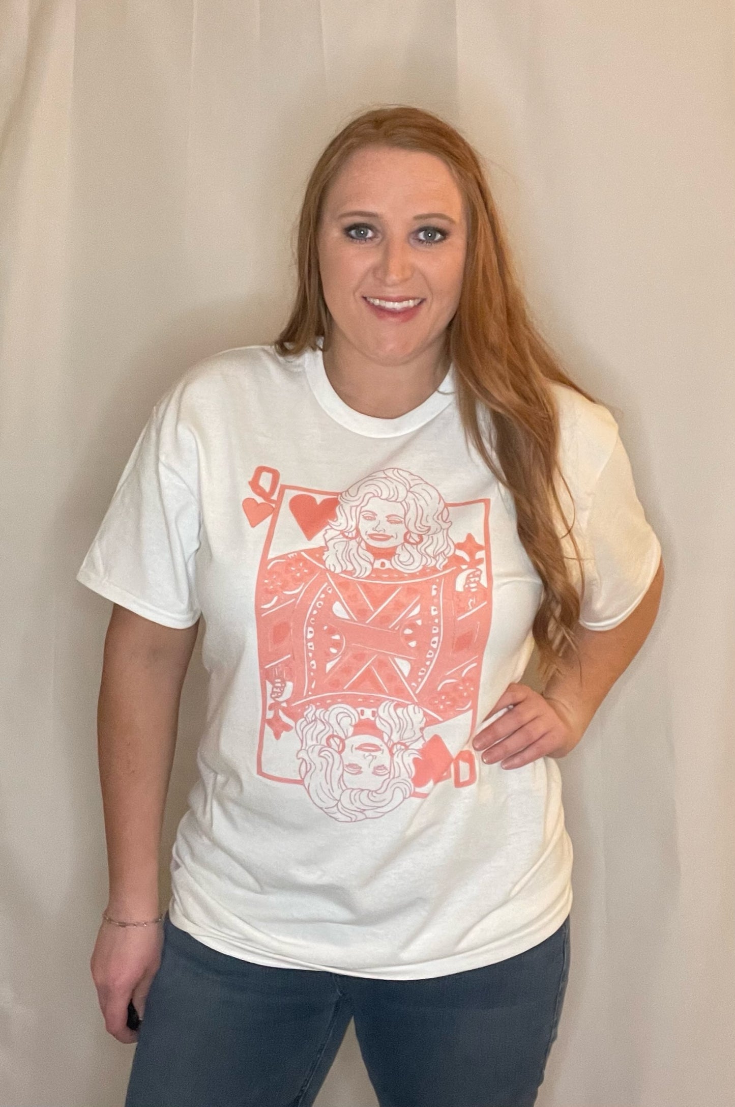 Woman wearing White t-shirt with queen of hearts playing card graphic in pink with Dolly Parton as the queen Edit alt text