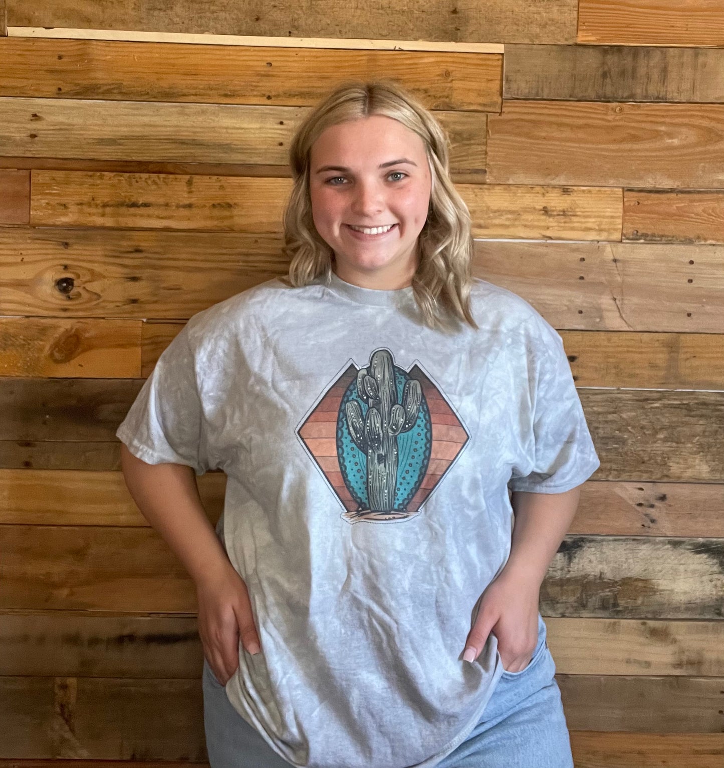 Model wearing Grey tie-dyed shirt with a Cactus on a Turquoise stone and yellow and rust striped background in an X-large