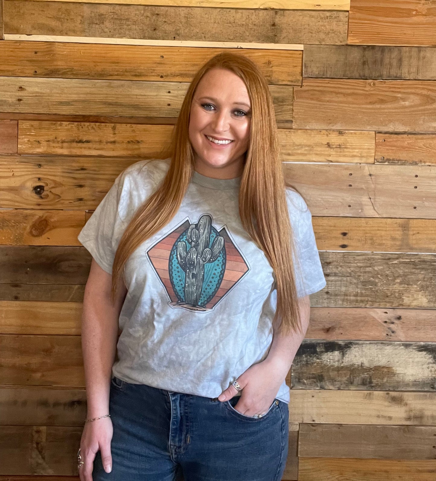 Model wearing Grey tie-dyed shirt with a Cactus on a Turquoise stone and yellow and rust striped background in a Large