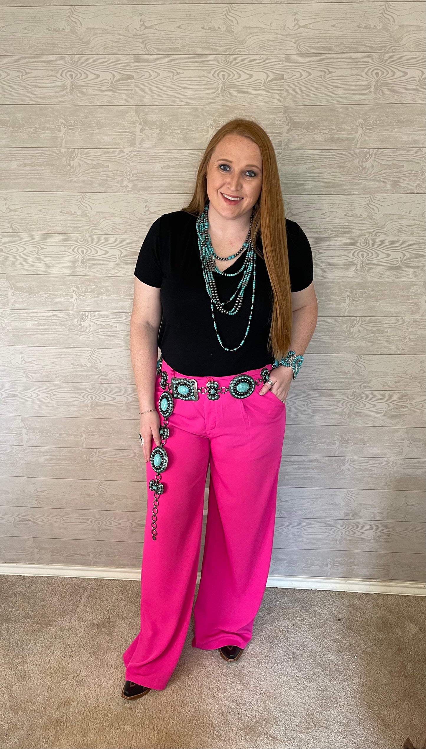 Model wearing pink wide leg pants with black shirt, turquoise necklace, turquoise belt, and black boots