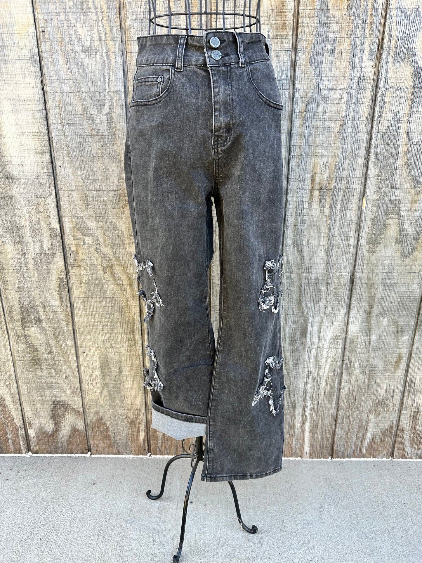 Black denim straight leg jean with distressed star patches on legs. 