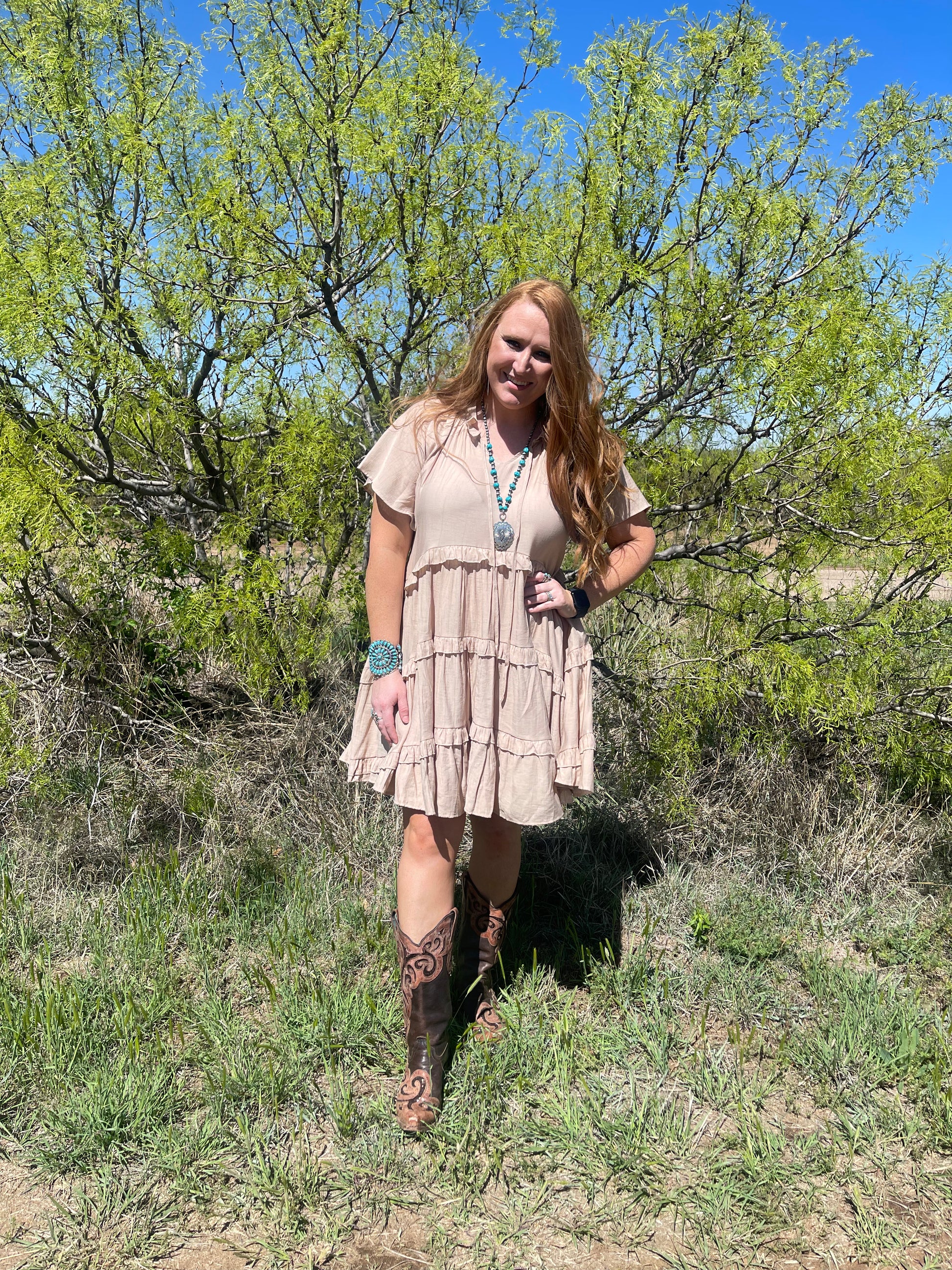 Model wearing ruffle tiered khaki dress with brown western boots 