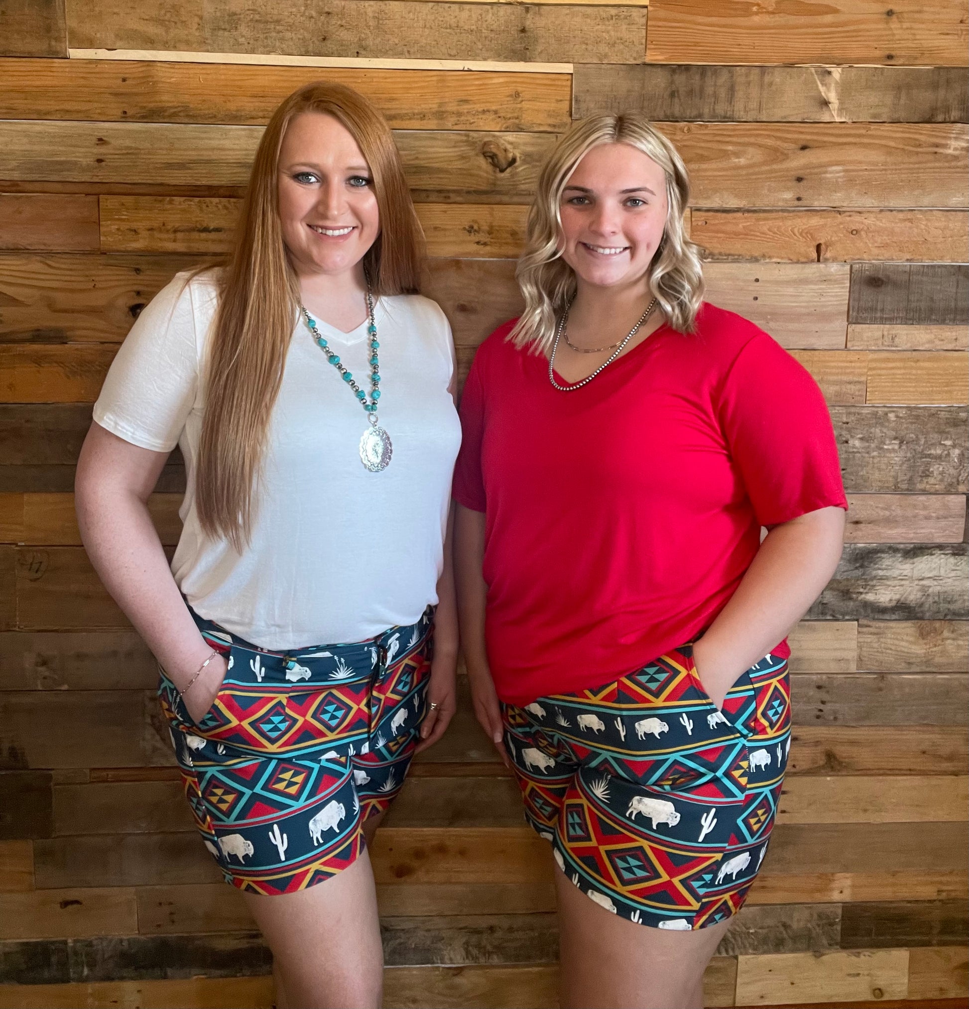 Two Models wearing tribal and buffalo print shorts, one with a red shirt and one with a white shirt. 