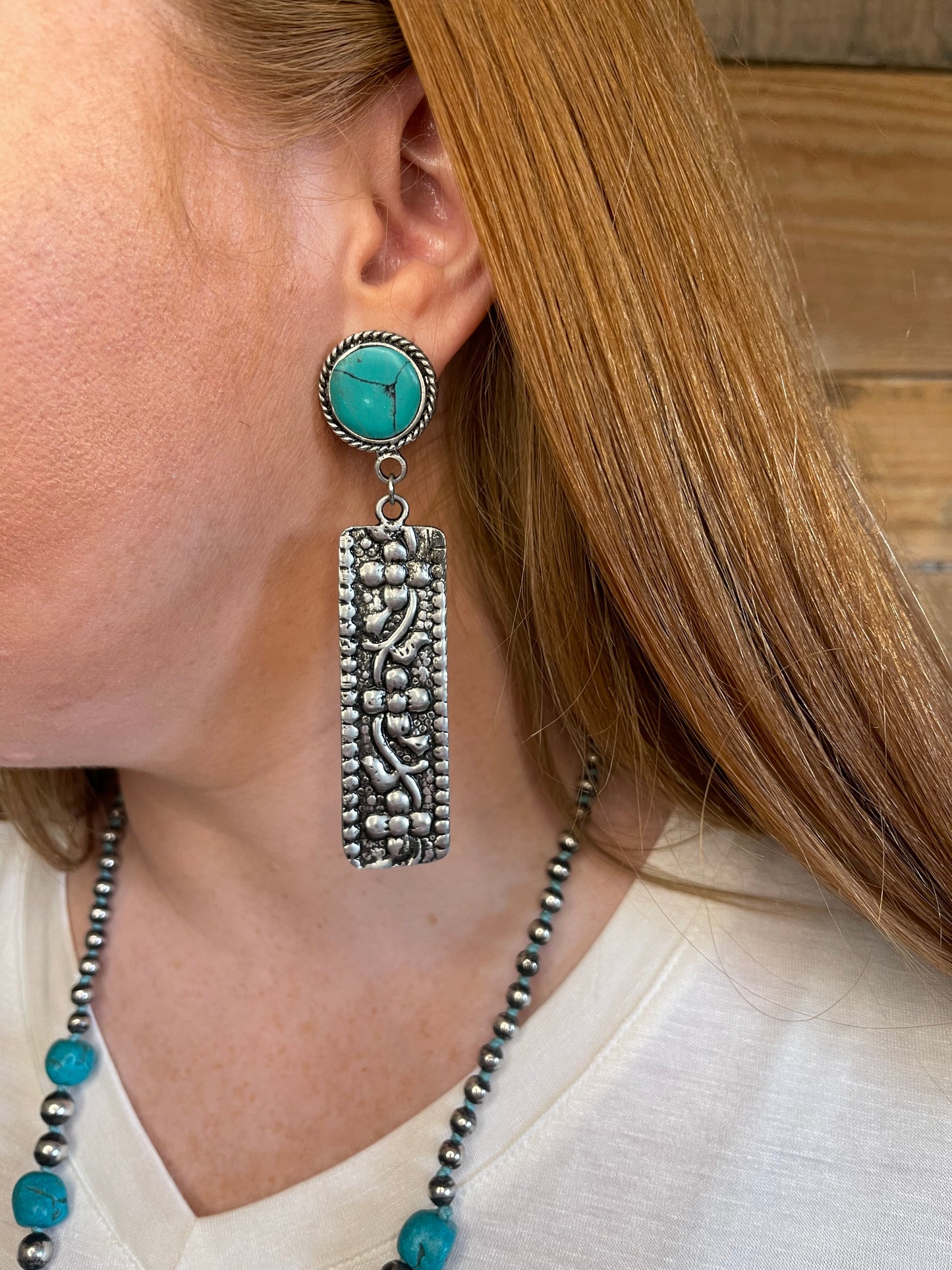 Woman wearing earring with turquoise stone and tooled silver bar